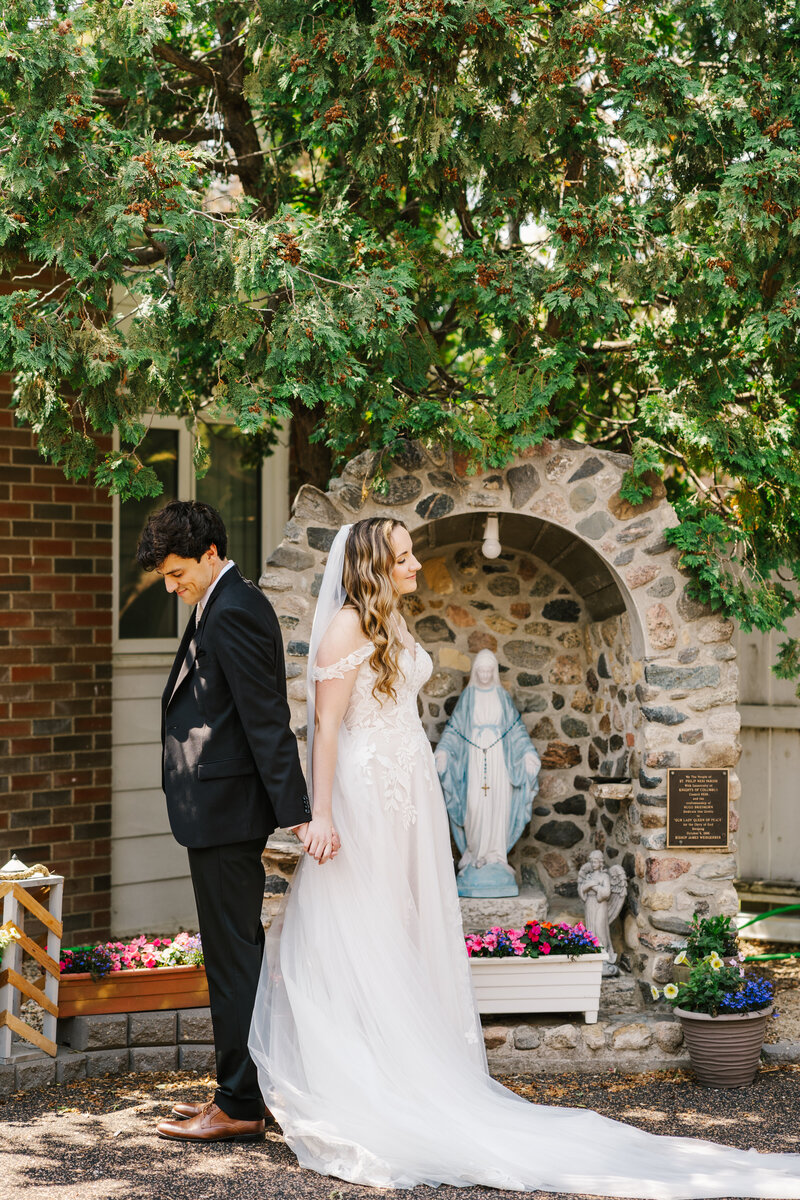 Bride and groom with their backs to each other holding hands under tree branches