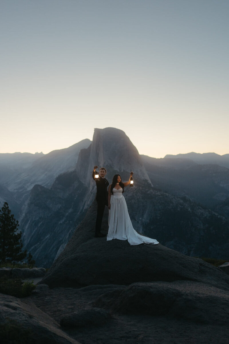 Bride and Groom are eloping in Yosemite at sunrise holding lanterns in front of Glacier Point