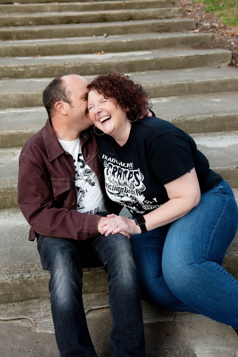 a hip couple wearing punk tshirts hug and laugh while sitting on some steps