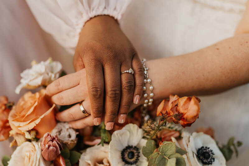 Two hands resting on a bouquet of flowers showing off wedding rings 
