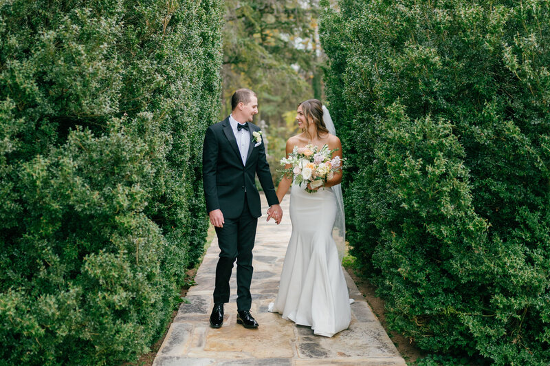 a bride and groom holding hands while walking in a garden