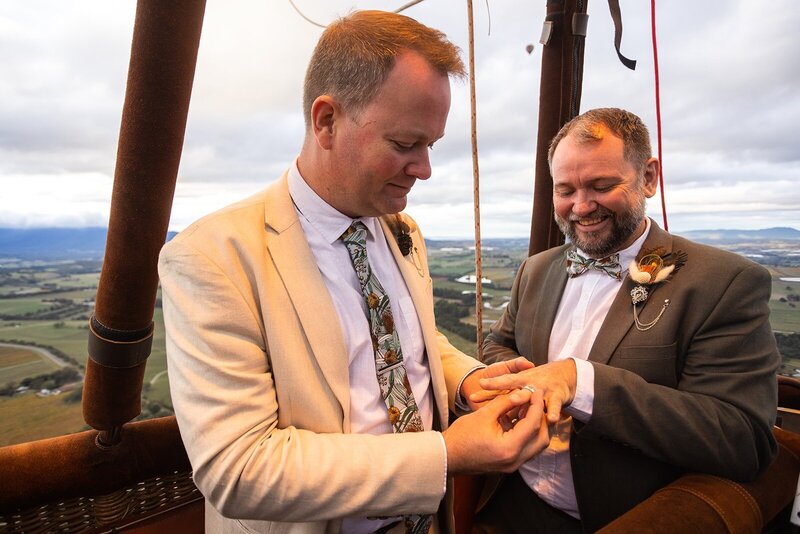 Two men exchanging rings at their elopement in a hot air balloon over the yarra valley.
