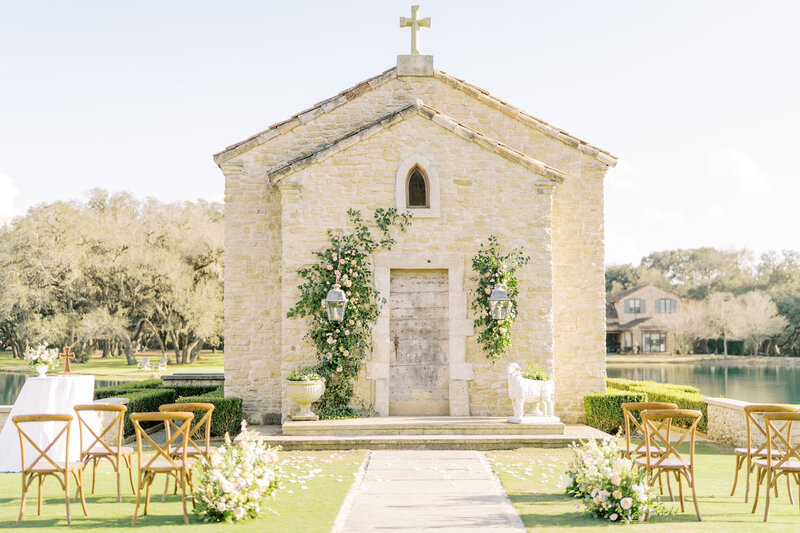 Outdoor photo of a stone chapel building and ceremony chairs decorated with greenery