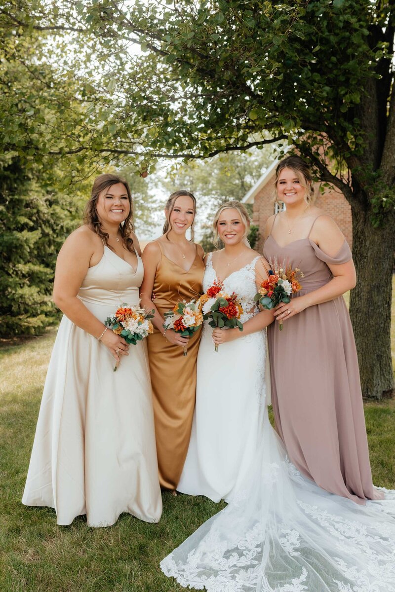 Natural light wedding photography in Michigan featuring bride and bridesmaids with warm, earthy-toned dresses and florals.
