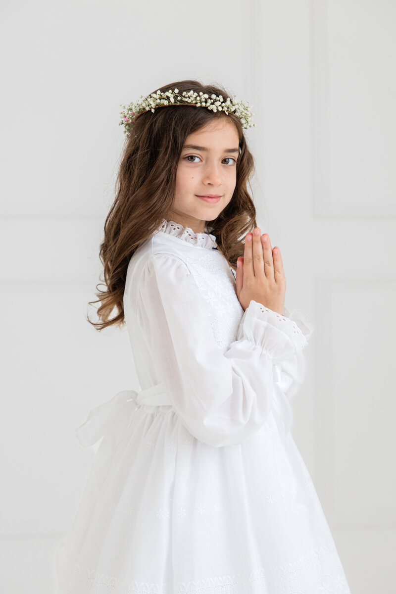 Young girl in white dress and flower crown posed with hans together in prayer.