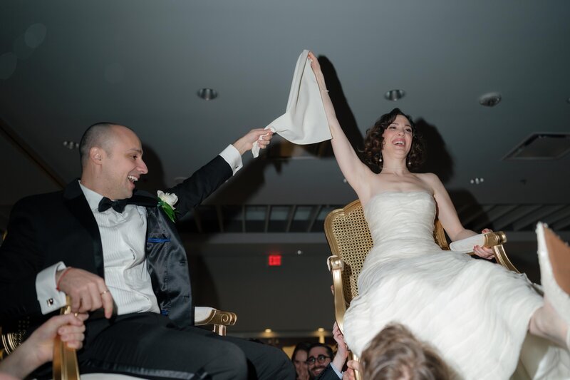 A couple in their wedding outfits hold hands, smiling
