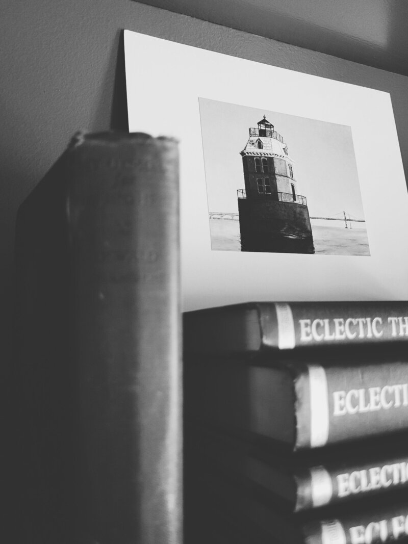 White lighthouse print on books sitting on a bookshelf