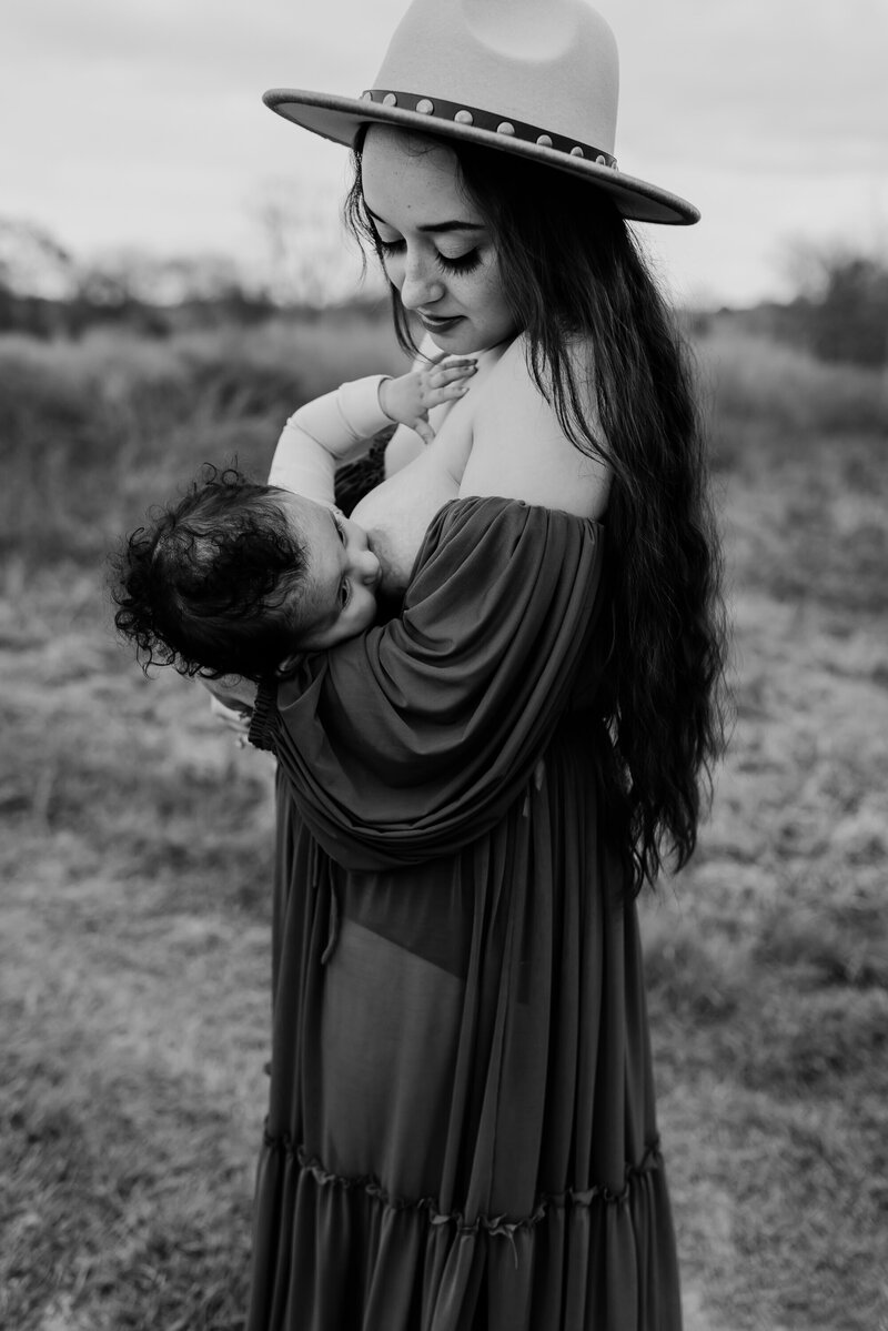Mother breastfeeding her baby in a grassy field, wearing a wide-brim hat, black-and-white photo in Macon, GA.