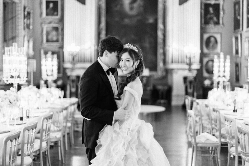 Black and white image. Bride in a Monique Lhuillier dress and groom at their fine art style wedding inspired by Bridgerton at Somerley House, surrounded by elegant decor.