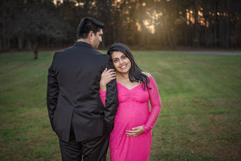 An Indian couple posing for their maternity photoshoot. The woman is in a bright pink maternity dress.