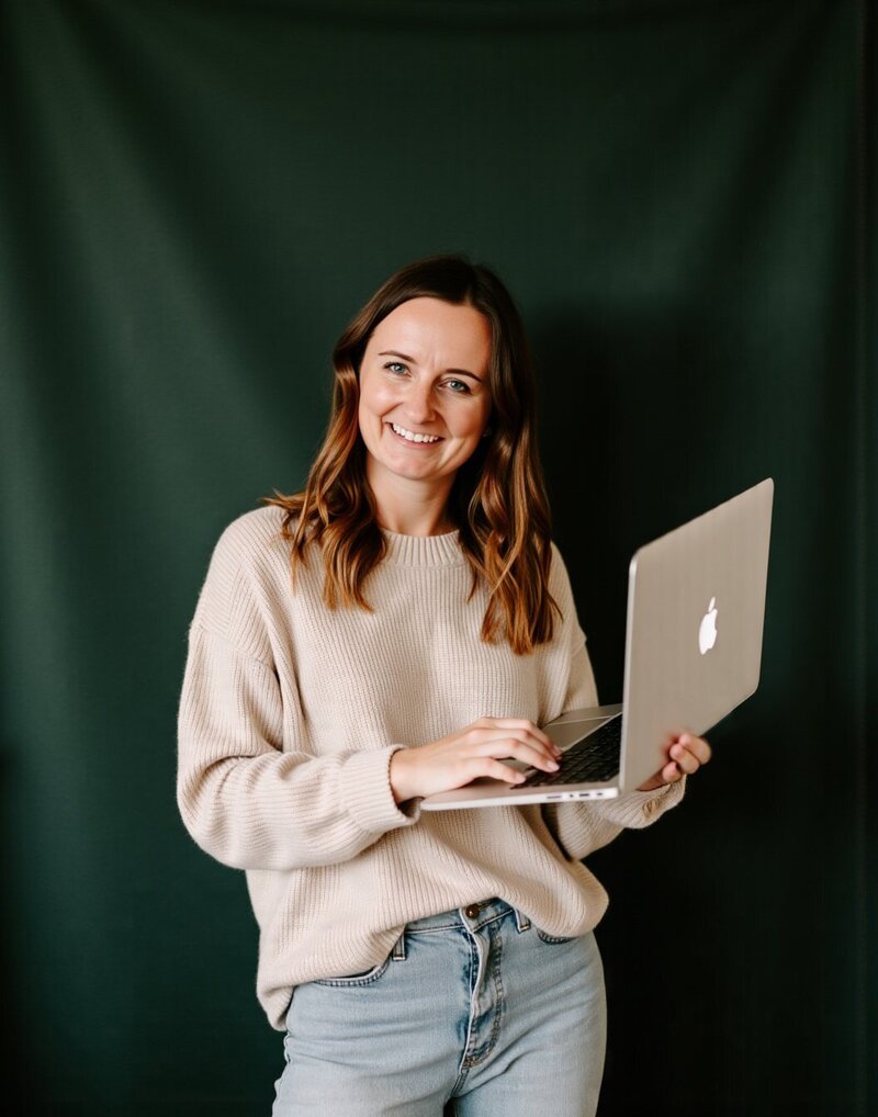 A woman named Jordin, owner of Unica Formo, smiling while holding a laptop, showcasing a positive and engaging expression.