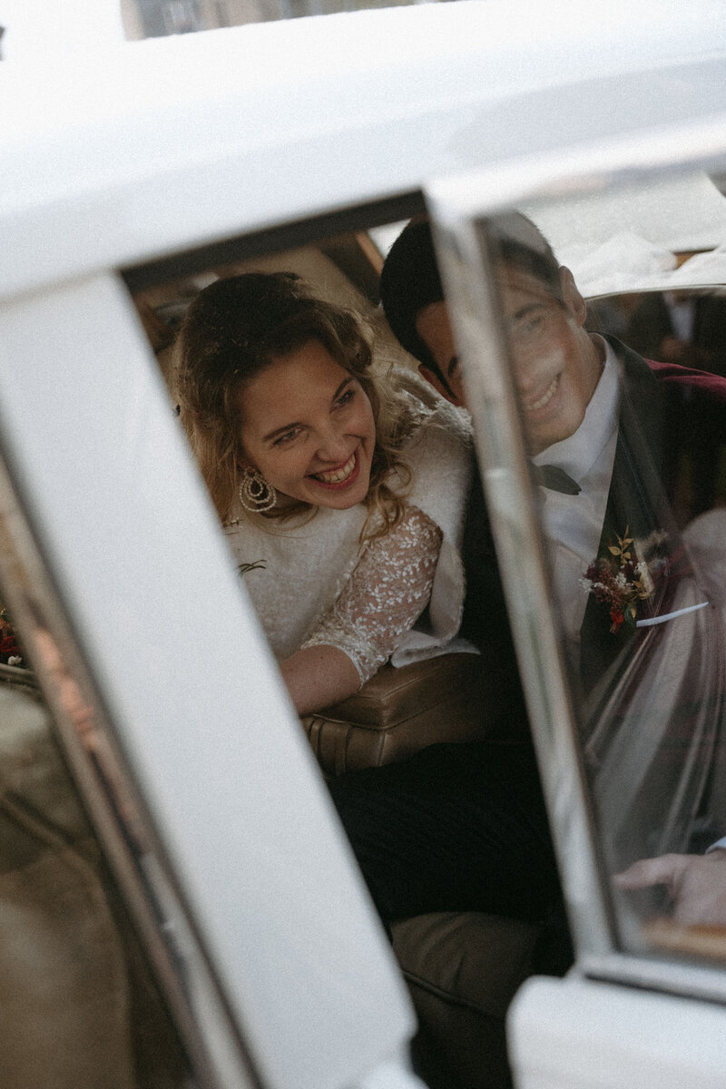 Mariés assis sur la banquette arrière d'une voiture vintage blanche au Château de la Rouerie. Par Kamescop photographe de mariage en Bretagne et ailleurs.