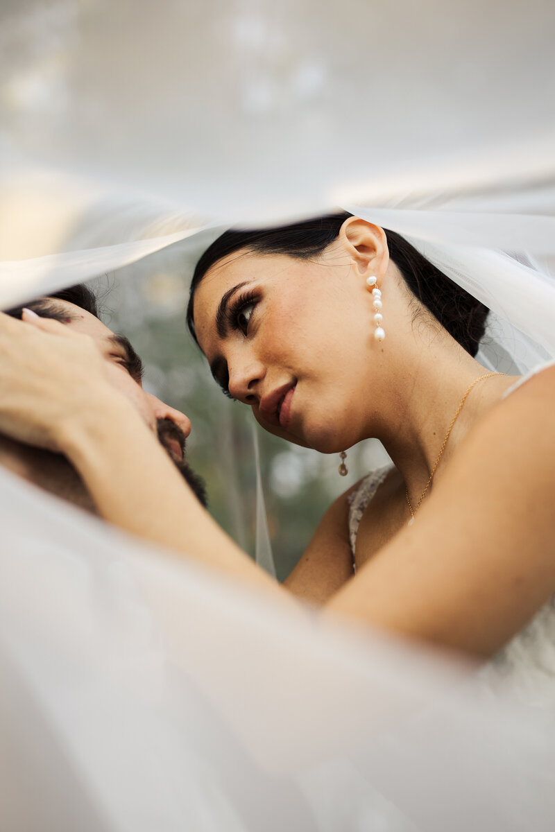 Bride and groom cupping each other's faces with their hands, under the veil