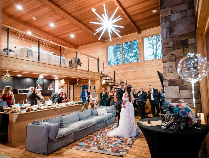 A bride and groom pick items from a beautiful wooden luxury charcuterie tray provided for them at the luxury glamping camp on the Matanuska glacier during their Alaska Glacier Elopement.  This special inclusion  is part of their inclusive elopement package, and you can see the bride's lacy dress in the background of the tray.