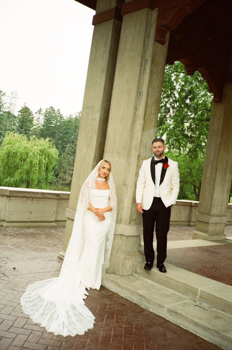 Bride and groom hugging and resting their foreheads together stand in lush green trees