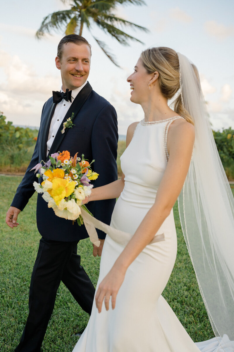 A happy couple just married walk away from their ceremony smiling and looking into each others eyes while she holds an incredible bouquet made by Natalia of Molly in the Sky.