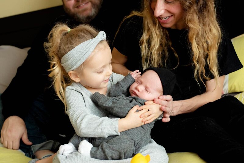 Mom and daughter hold the new sleepy baby brother.