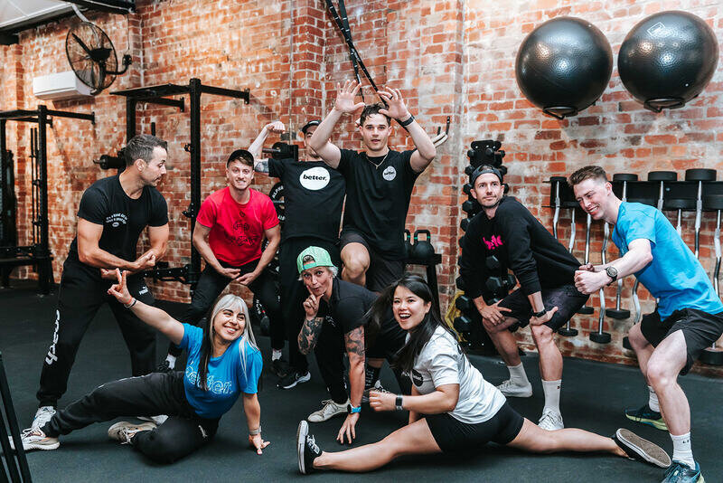 Project Better Team Posing in Gym: Members of the Project Better team striking playful poses in a gym with a modern industrial brick-wall interior.