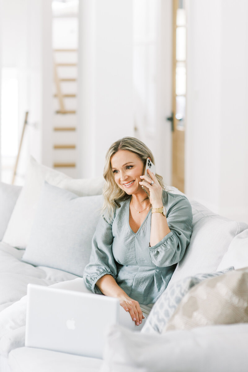 Top London Ontario interior designer and decorator sits in her luxury living room smiling as she talks on the phone with her client.
