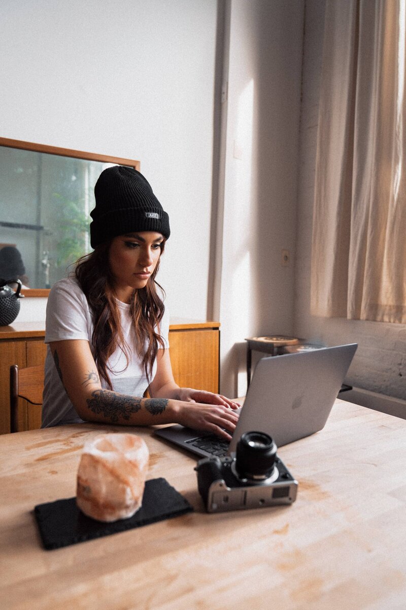 Tattooed woman at a desk with a camera and a laptop