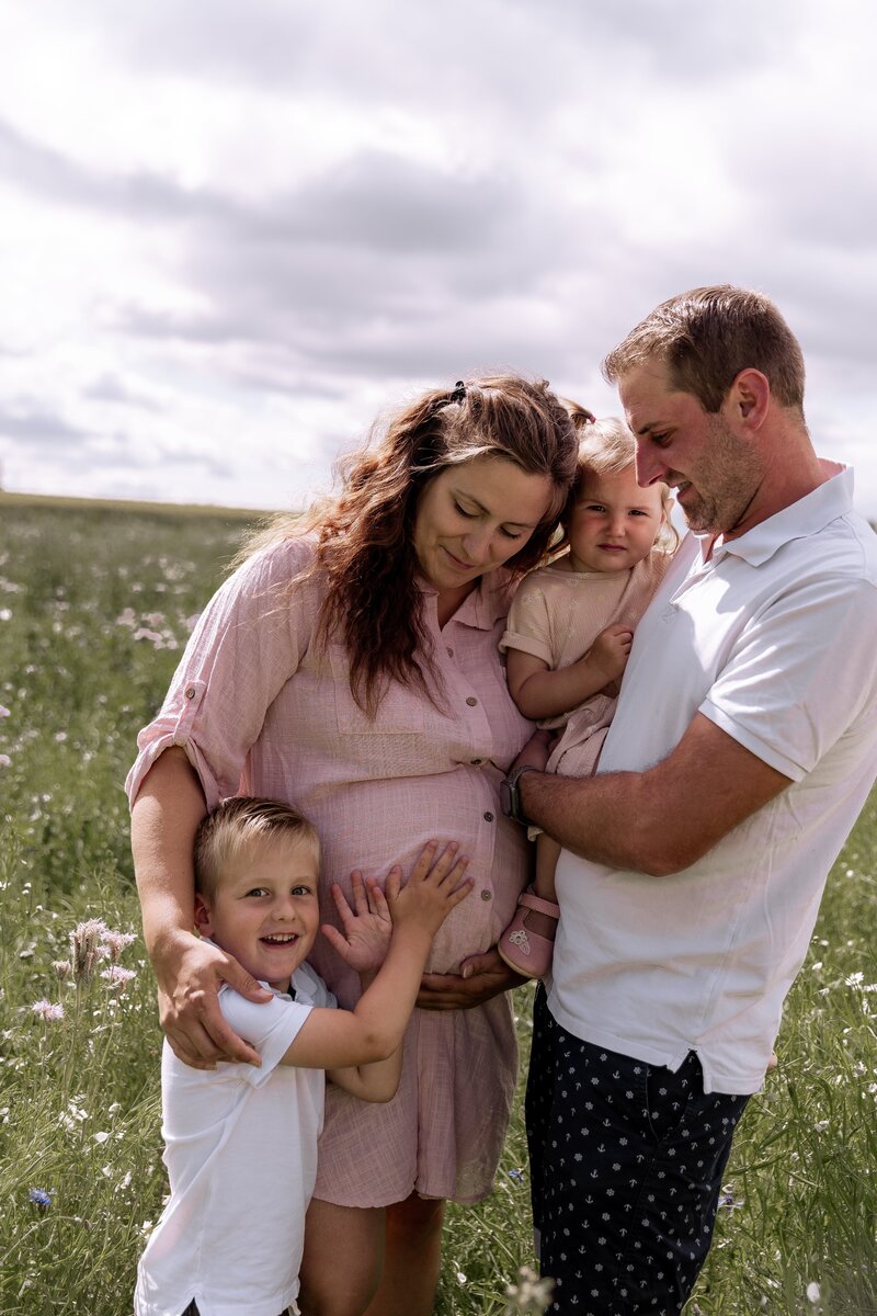 Mutter Vater und zwei Kinder stehen Arm in Arm auf einer Wiese