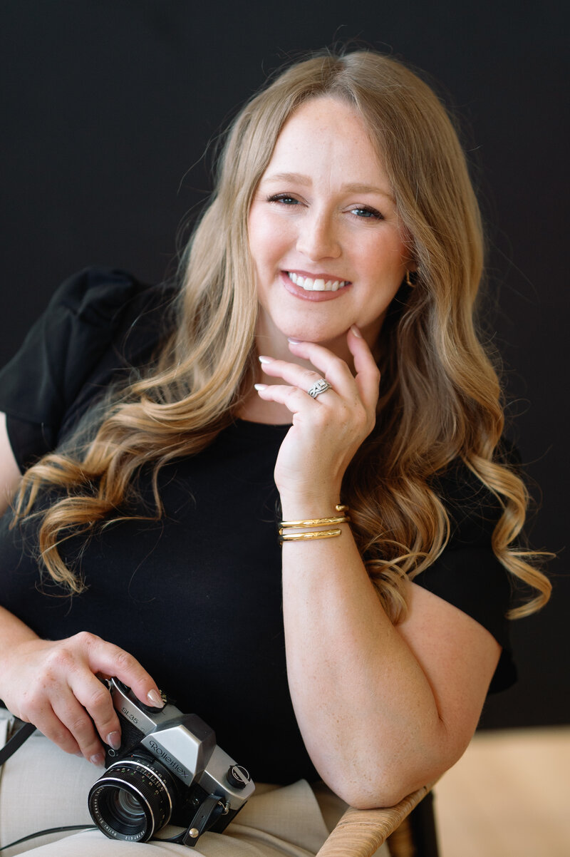 Courtney Paige smiling headshot holding camera, long curled hair, black top | Ohio wedding photographer