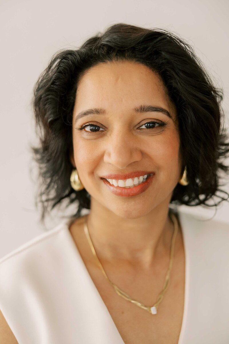 Beautiful Indian woman wearing gold jewelry and an all white outfit and smiling at the camera