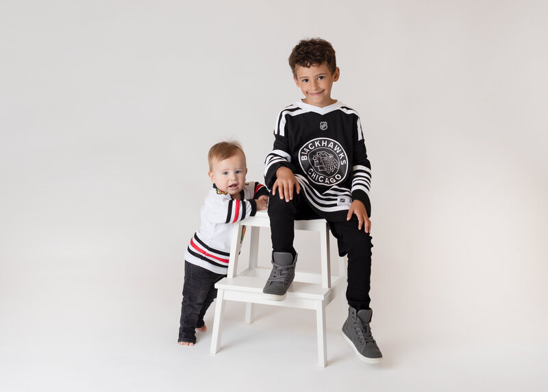 Two brothers wearing Chicago Blackhawk jerseys with white stool