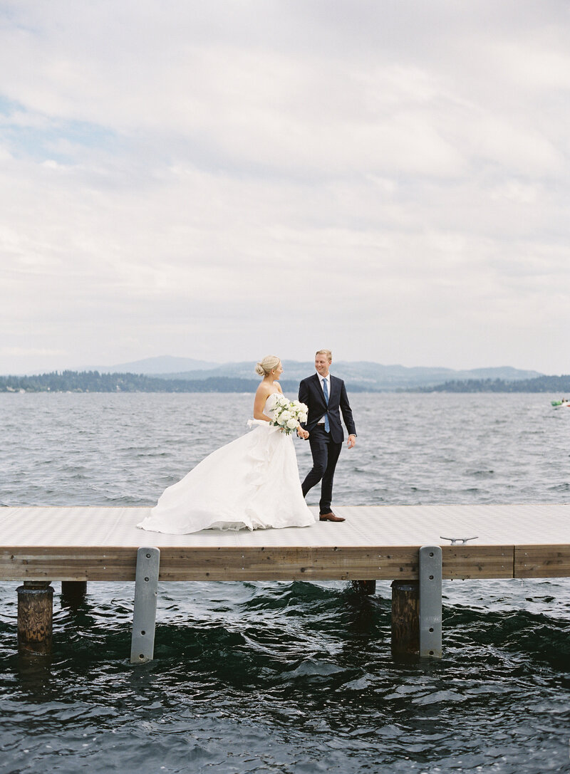 Seattle Wedding Photographers -bride and groom in black and white sitting on a dock at the lake in the evening looking towards each other