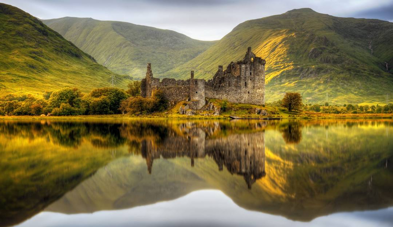 Loch-side castle ruins reflecting in calm water, evoking a mysterious literary landscape inspired by Kat MacKenzie's 'Work In Progress'