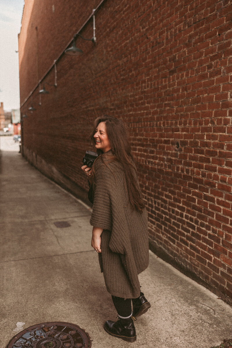 Photo of RVA photographer during branding session. Walking in brick alley.