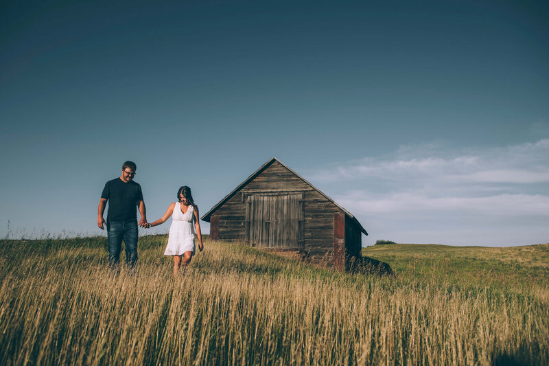 couple walks in field of tall grass with barn in background