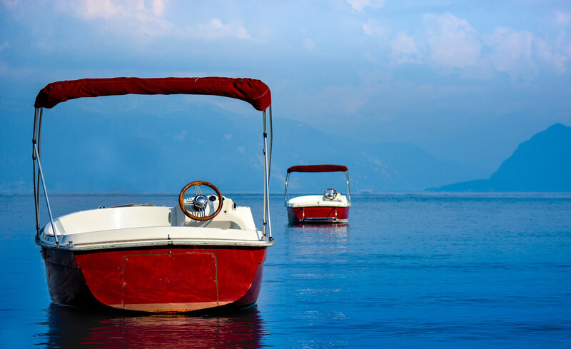Two red boast float out on a lake in the Swiss countryside overlooking a hazy mountain range.