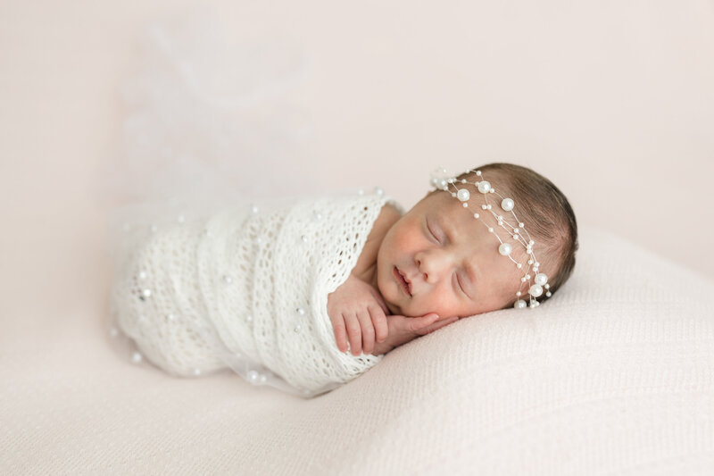 A newborn baby in a white wrap with pearls being photographed by a newborn photographer in Midland Michigan