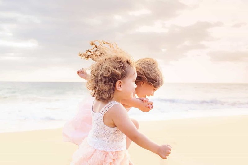 children holding hands as they run together on the beach with the wind in their hair