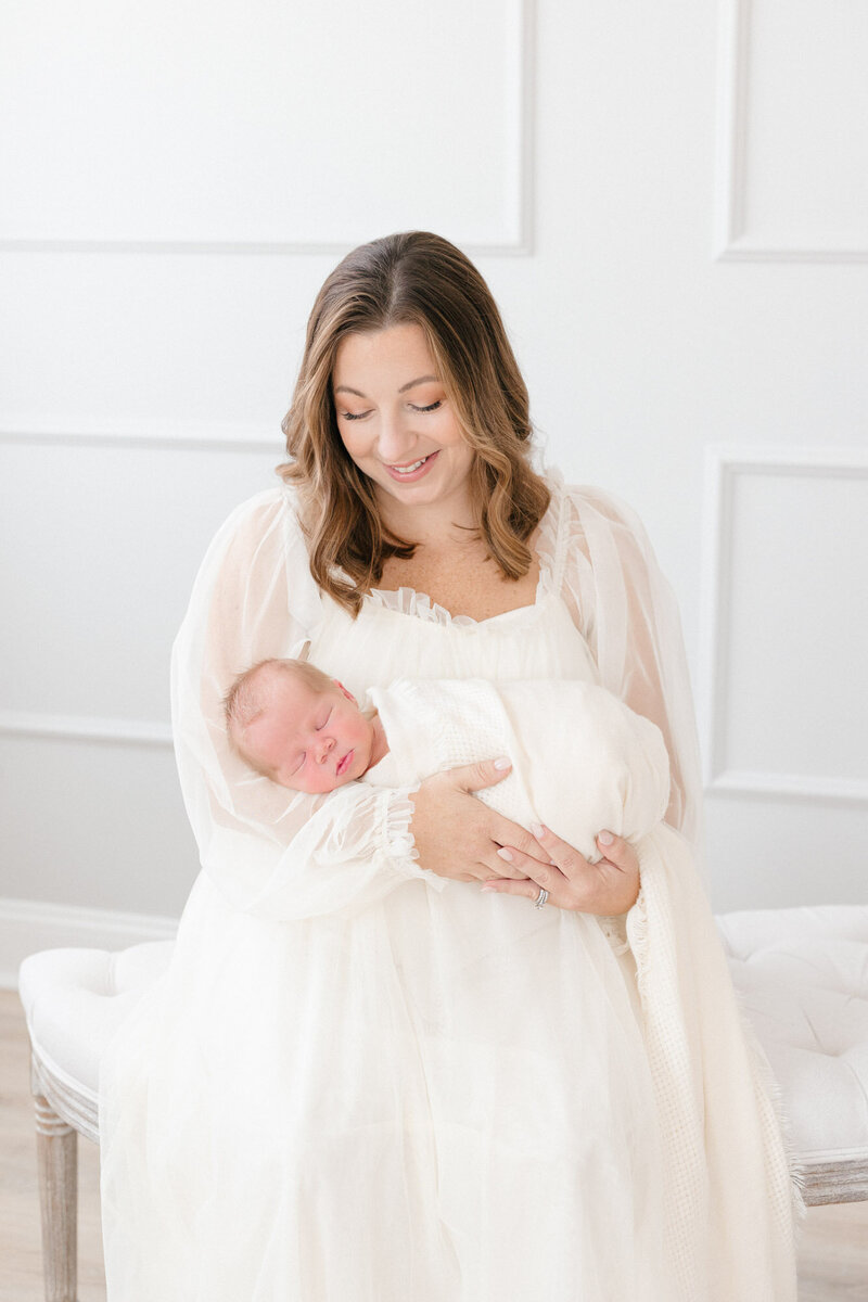 Mom smiling at her toddler while holding her newborn baby boy in a bright, warm Louisville KY photography studio