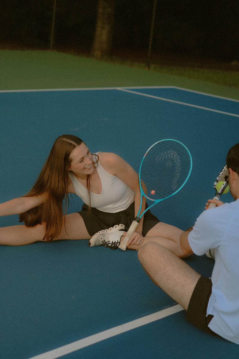 A couple are seen stretching on  a tennis court while their rackets are next to them.