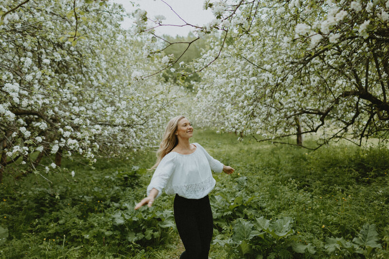 Muotokuva naisesta, joka pyörii ympäri hymyillen kukkivien omenapuiden seassa
