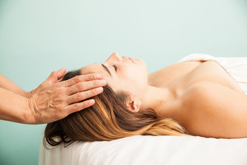Mains posées sur la tête d'une femme allongée sur le dos recevant un massage énergétique à Challans en vendée.