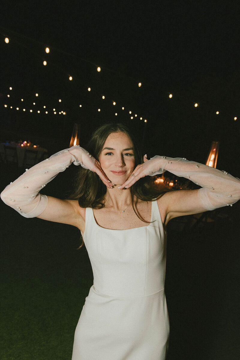 Bride posing with pearl sheer gloves at night outside with festoon lights behind her