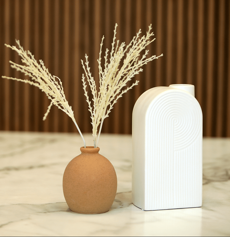 Small vase with dried plants beside a white vase