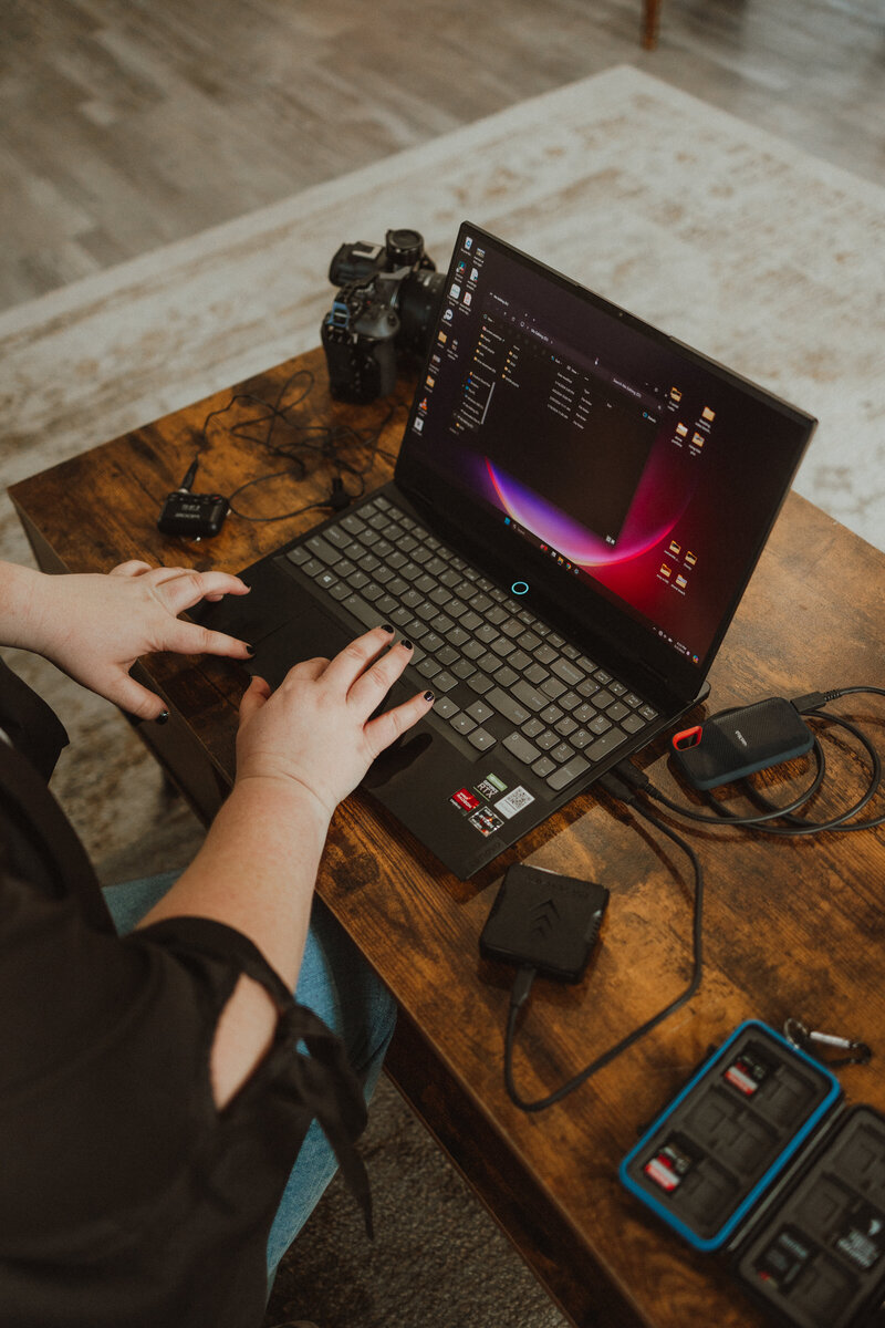 laptop open on a wooden table with cables plugged in to transfer footage. 