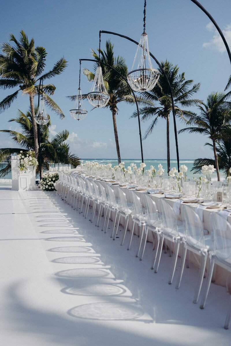 Perfectly lined up chairs at a beach wedding table with chandeliers and playful shadows