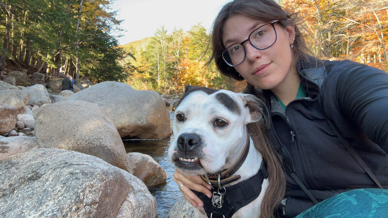 Image of Grace LeBlanc and her pitbull Winnabow, sitting on rocks in a riverbed in North Conway, New Hampshire.