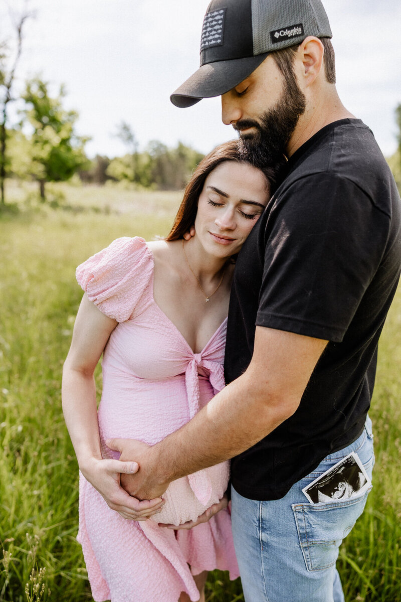 Couple maternity portrait in natural light with partner’s arms wrapped around her belly and her head on his chest in Farmington, Missouri. 