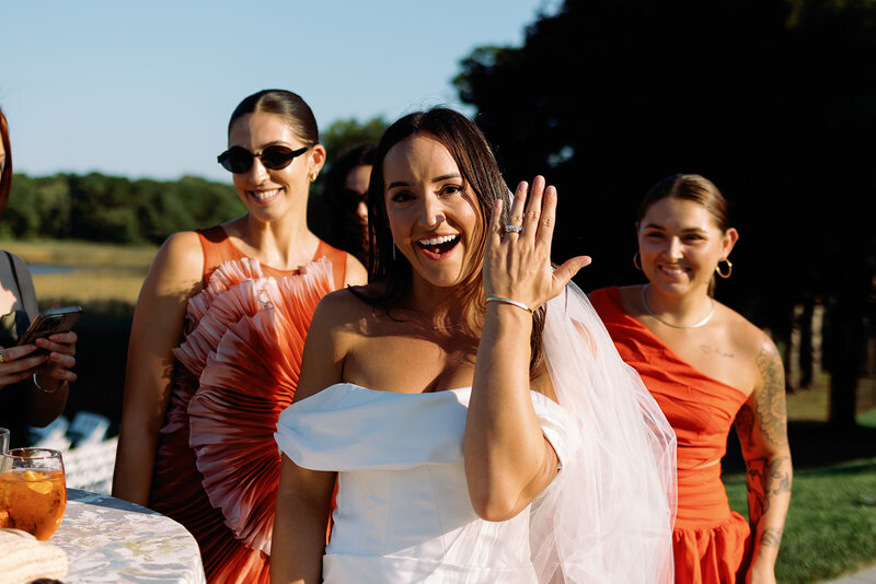 Stunning bride with friends in bright dresses holding up her hand with wedding ring