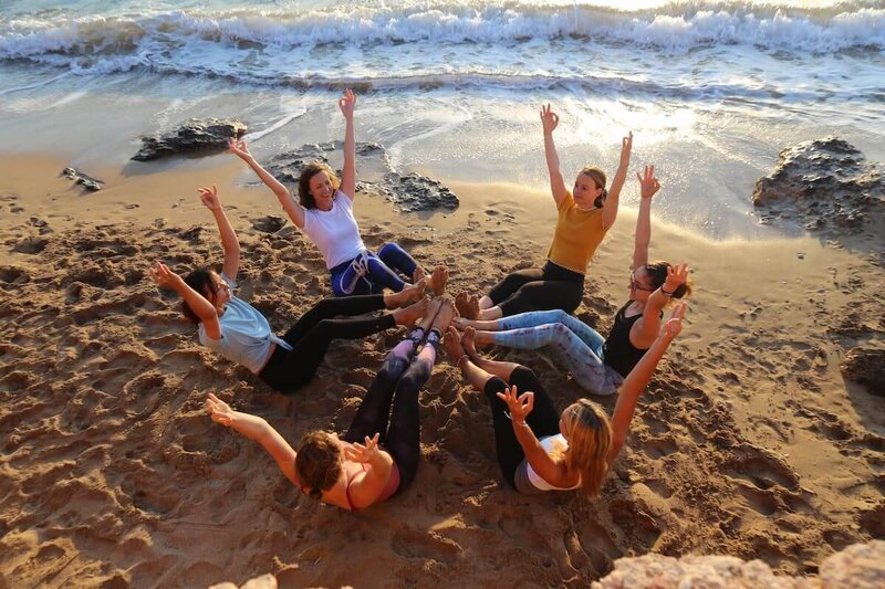 Graduates celebrating in a joyful boat pose circle on the sand.