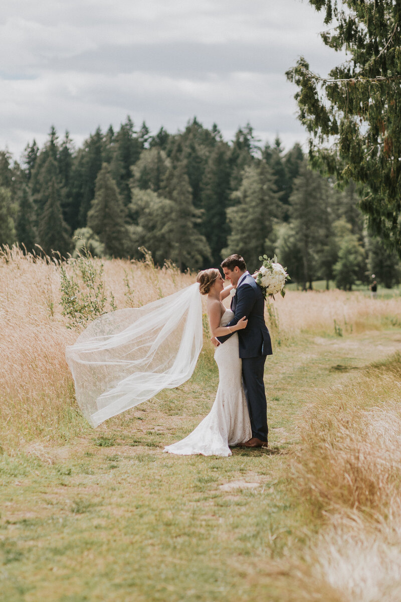 real bride wearing a floor length veil blowing in the breeze and posing with her groom in a field