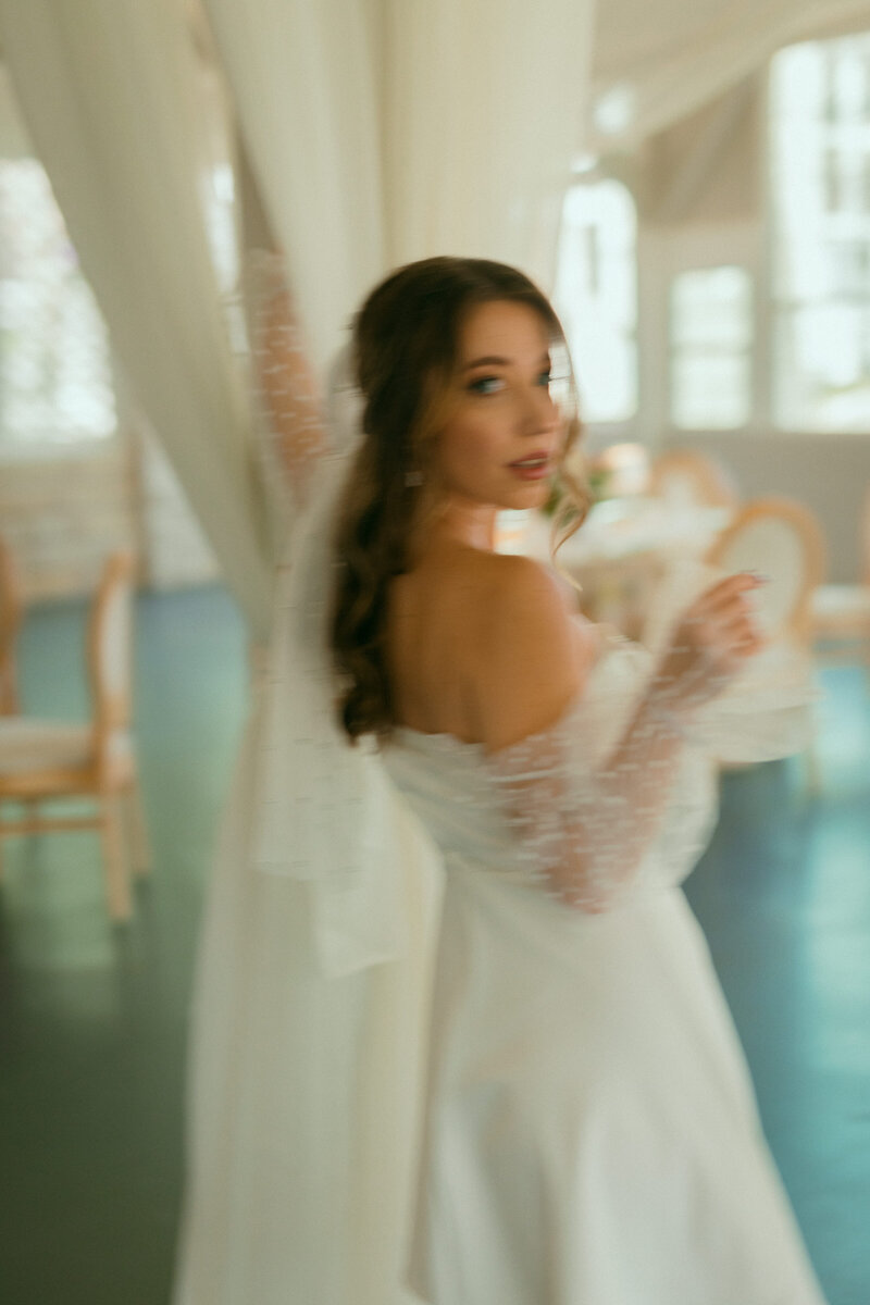 Bride in off-the-shoulder lace wedding gown twirling in a light-filled venue, surrounded by romantic floral decor designed by Eventive Designs in Austin, Texas.


