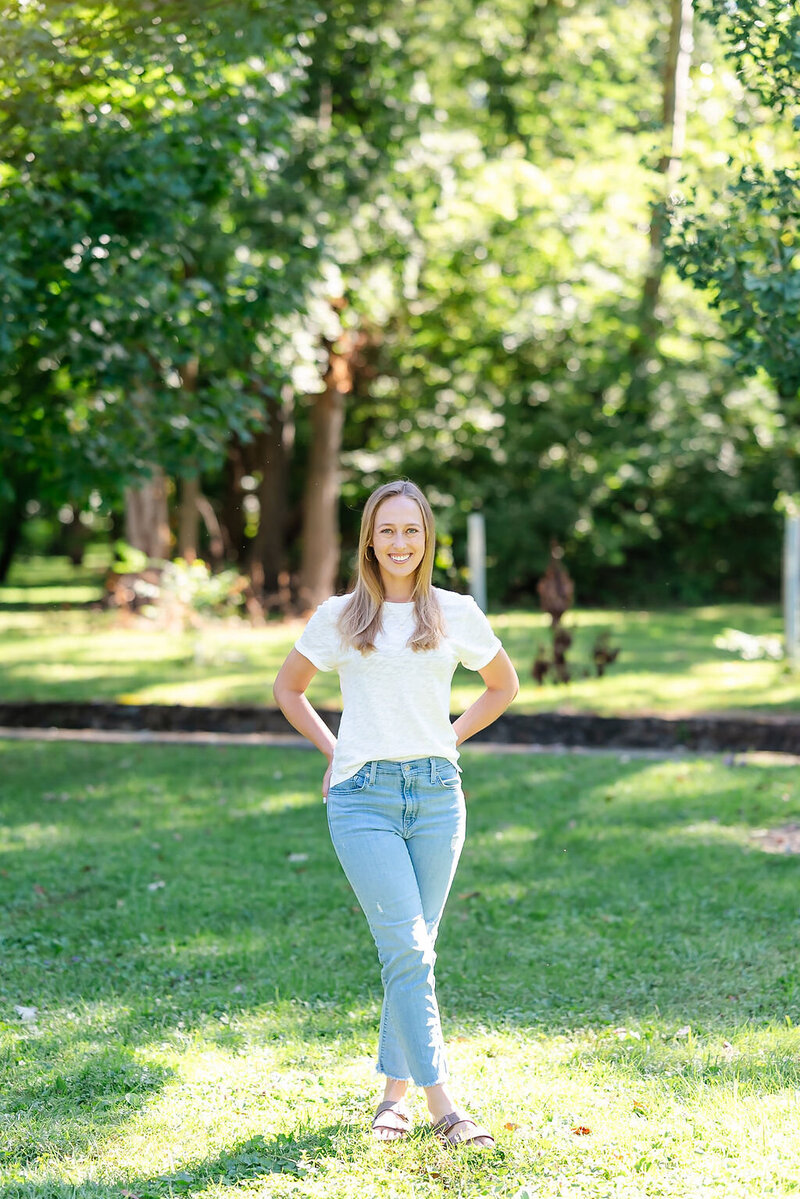 Portrait of Emily Howell wearing a white t-shirt and jeans, standing in a park